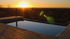 Une terrasse en bois offrant une vue dégagée sur le coucher de soleil au-dessus d’un paysage vallonné.