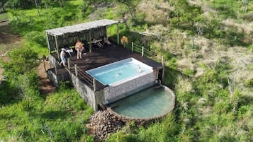 A hot tub with a stone surround, a wooden deck, and a thatched-roof structure.