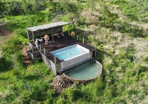 A hot tub with a stone surround, a wooden deck, and a thatched-roof structure.