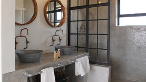 Une salle de bain avec deux grands miroirs ronds, une fenêtre à cadre noir et un lavabo en métal avec un bac.