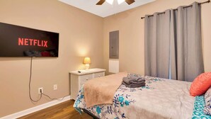Un dormitorio con cama, televisor montado en la pared, ventilador de techo y ventana con cortinas.