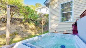 Un jacuzzi en un patio trasero con cerco de madera, una casa al fondo y una guirnalda de luces.