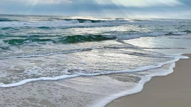 Una playa con olas y cielo nublado.