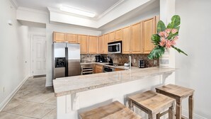 Una cocina moderna con armarios de madera, un refrigerador de acero inoxidable, un microondas y una encimera de mármol.