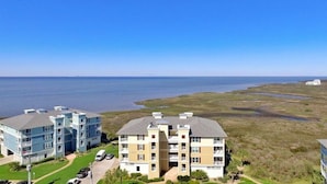 A multi-story hotel with a flat roof, located near a coastal area with a view of the ocean. - Newly renovated Bayfront Condo, Beach Club, Pools, Hot Tubs, Sunsets and More!! (Galveston)