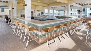 A bar area with a long counter and multiple bar stools, a large island with a sink, and a view of the ocean. - Newly renovated Bayfront Condo, Beach Club, Pools, Hot Tubs, Sunsets and More!! (Galveston)
