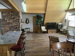 Relax in this spacious loft-style living area with a high ceiling and exposed beams, featuring a dining table, comfortable seating, and a flat-screen TV.