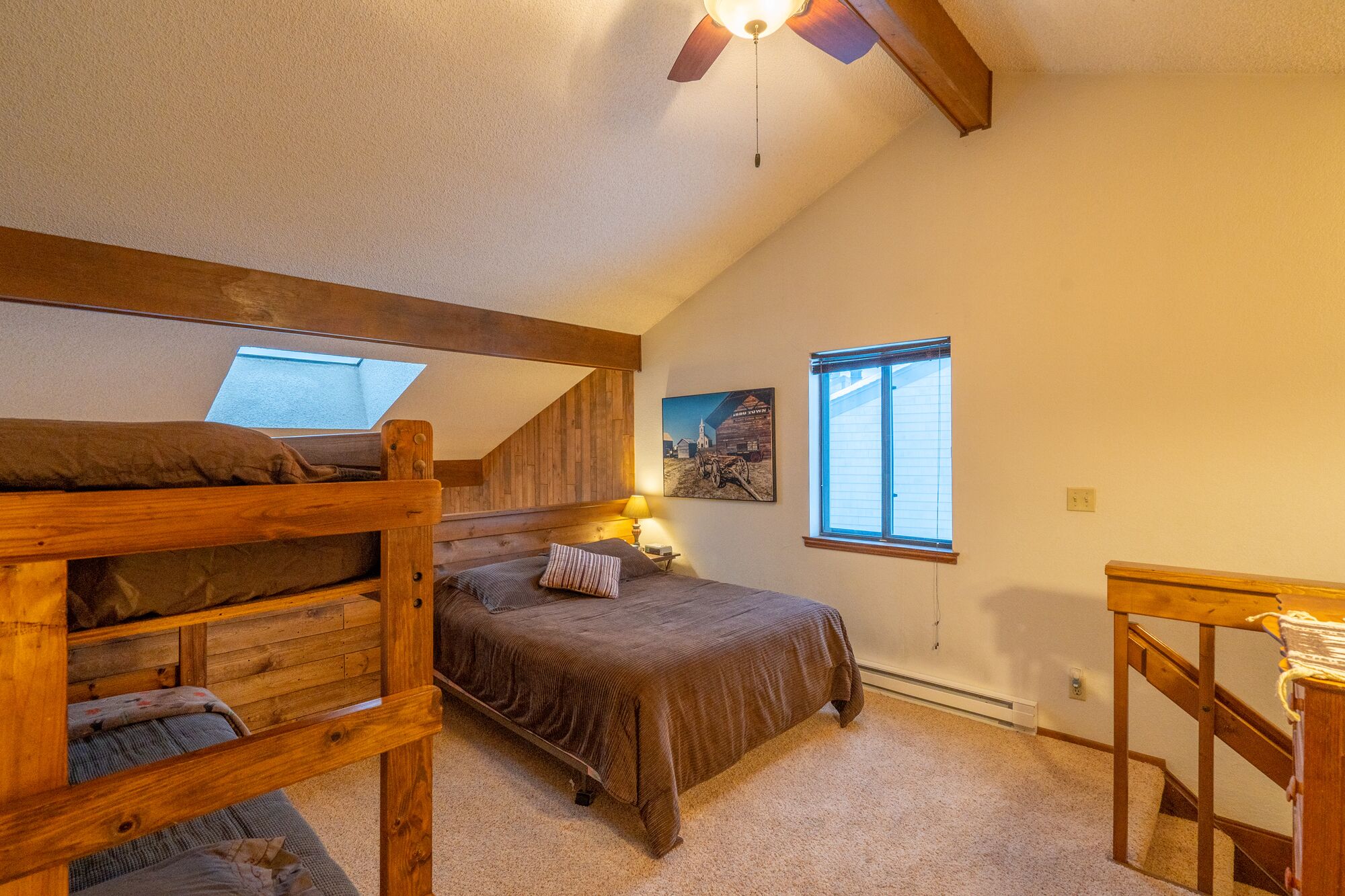 A cozy attic bedroom with a bunk bed, a single bed, a desk, and a window.