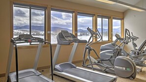 Ein Fitnessstudio mit Laufbändern, Crosstrainern und Blick auf verschneite Berge durch große Fenster.