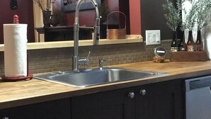 Een keuken met een spoelbak van roestvrij staal, een houten aanrecht en een achterwand van baksteen.