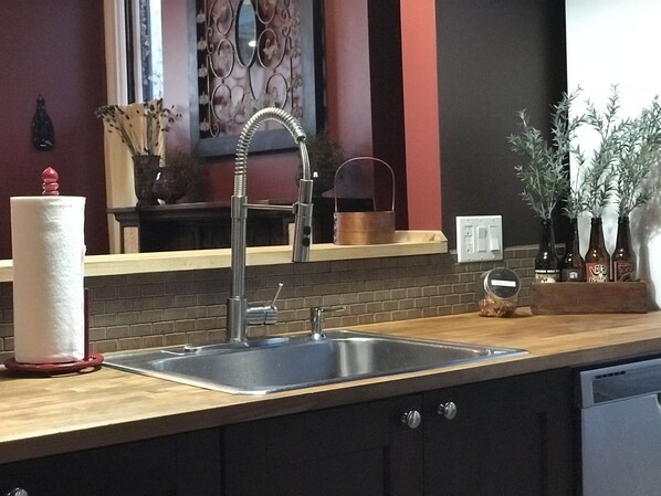 A kitchen with a stainless steel sink, a wooden countertop, and a brick backsplash.