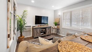 A modern living room with a flat-screen TV, a wooden entertainment unit, a sofa set, and a large window with blinds. - Wake Zone @ Lighthouse Lodge – Lake Views & Easy Water Access! (Kimberling City)