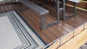Een overdekt terras met een houten tafel en bankjes, bakstenen muren en uitzicht op de omgeving.