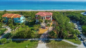 Une propriété située sur la côte, comprenant une grande maison et un bâtiment plus petit, le tout entouré d’une végétation luxuriante et offrant une vue sur la plage.