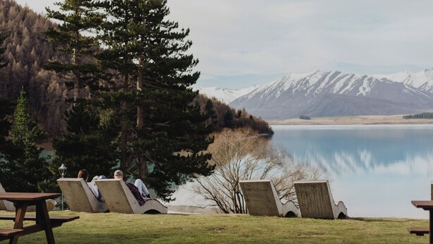 A lakeside view with chairs and a picnic table, surrounded by trees and mountains.