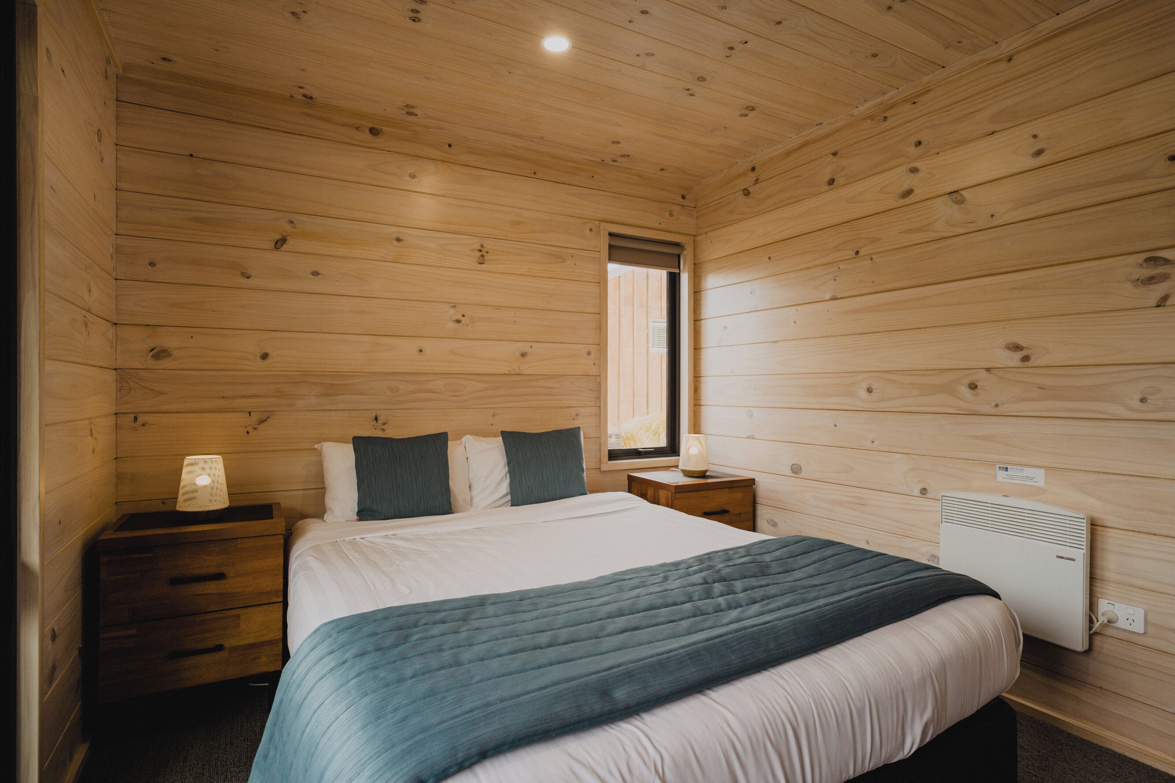 A wooden-paneled room with a bed, bedside tables, and a window.