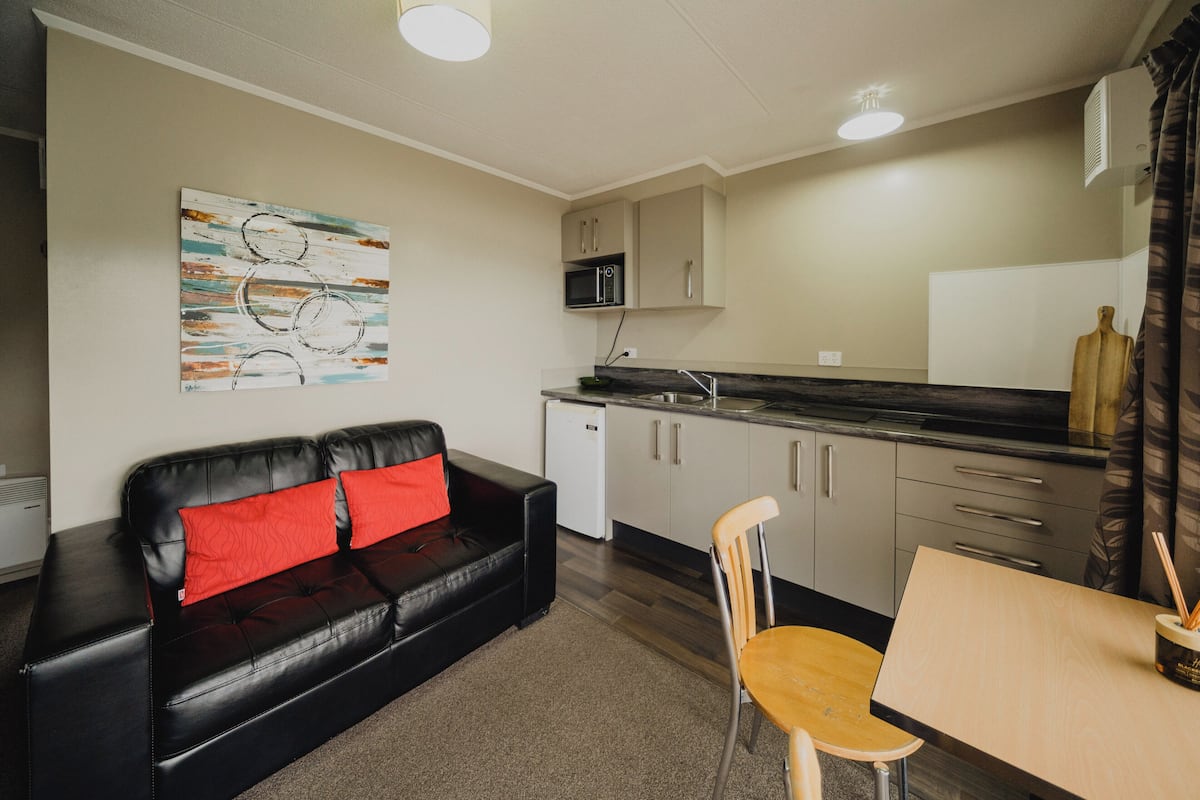 A compact living space with a black leather sofa, a wooden dining table, a microwave, and a small refrigerator.