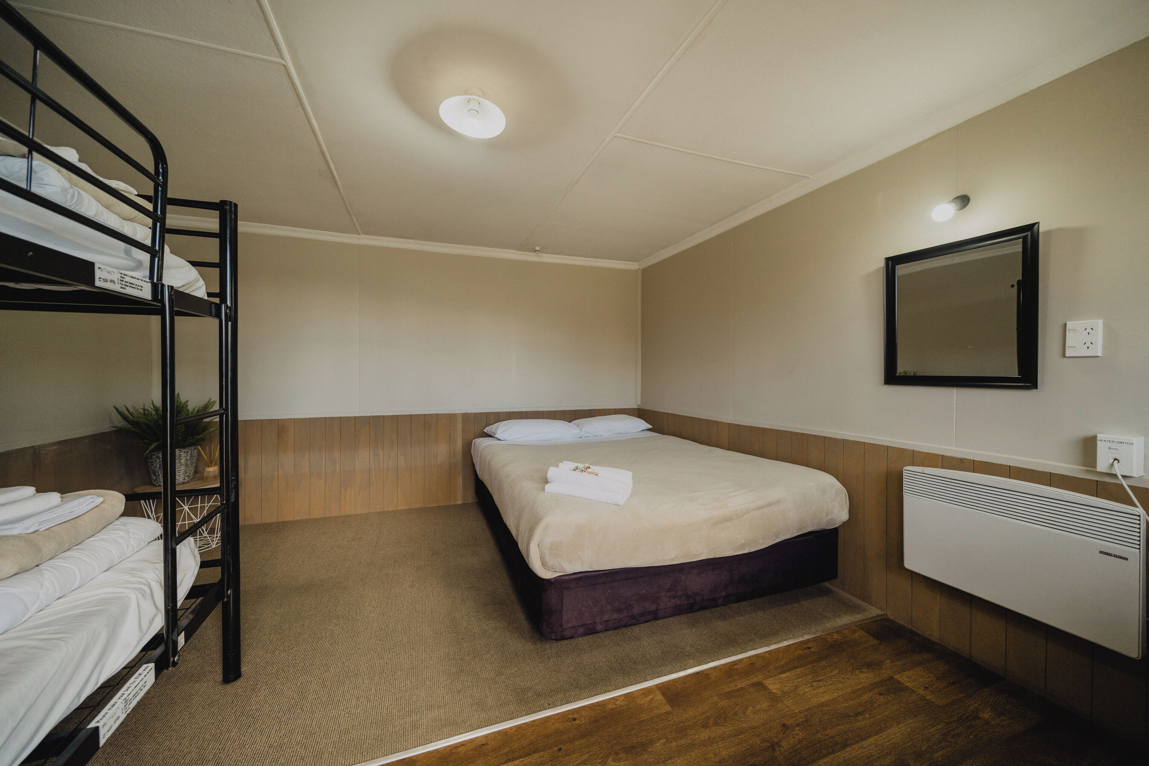 Een hotelkamer met een stapelbed, een eenpersoonsbed, een spiegel, een radiator en een kleine plant.
