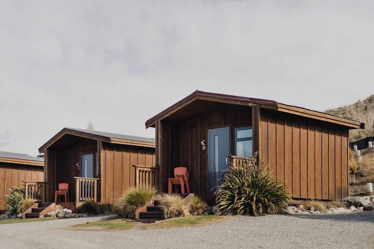 Two wooden cabins with a porch, a blue door, and a red chair.