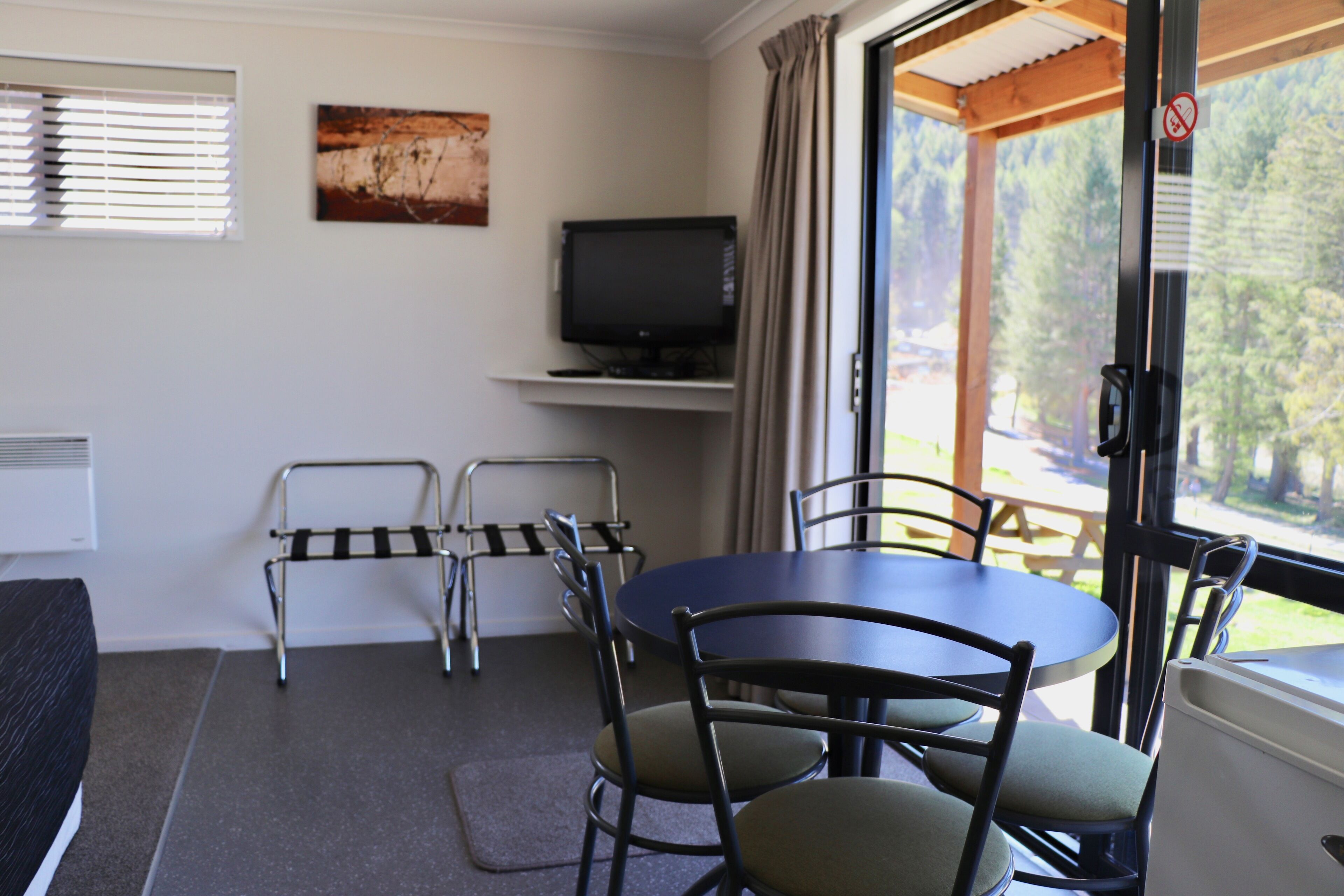 A room with a round table, chairs, a television on a shelf, and a window with curtains.