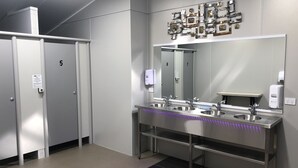 A modern restroom with three sinks, a large mirror, and a decorative wall piece.