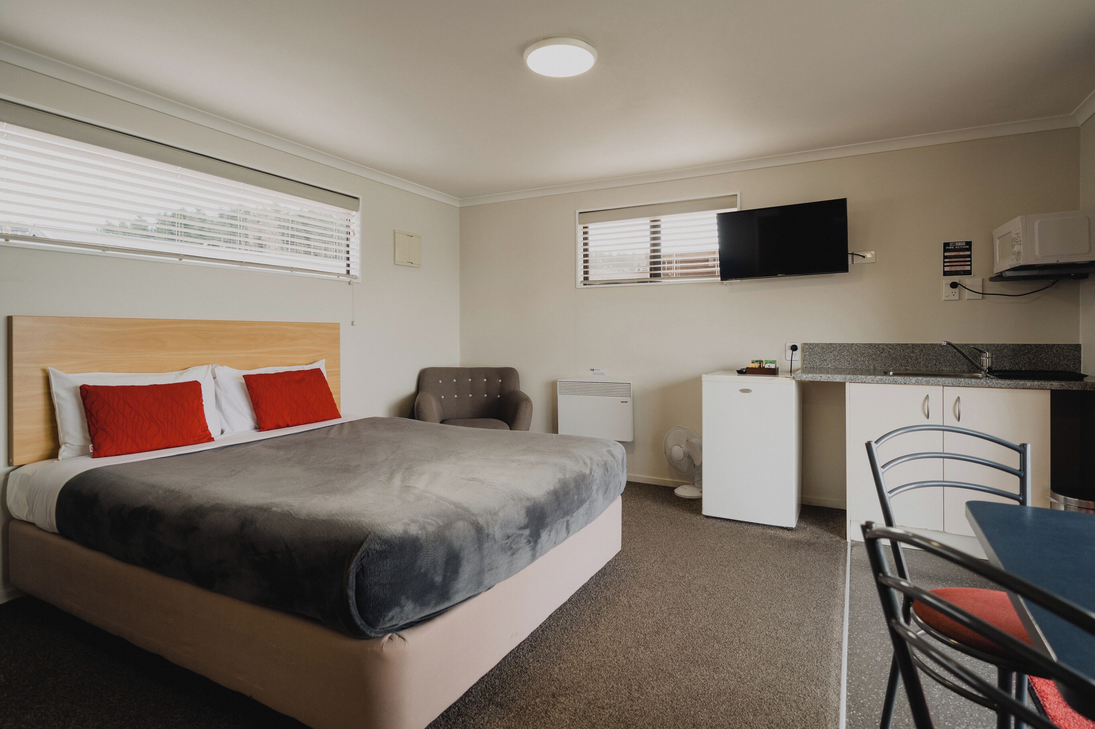 Un dormitorio con cama, escritorio, silla, televisor y kitchenette.