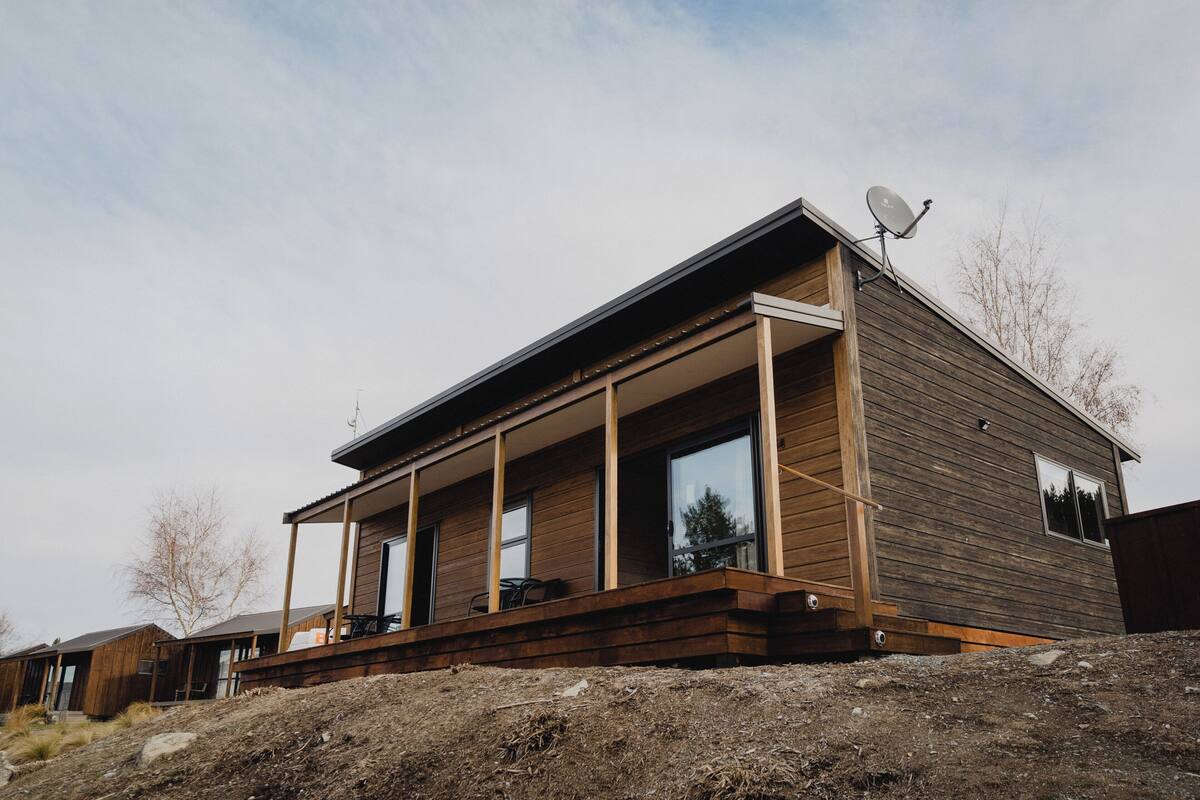 A modern wooden house with a balcony, large windows, and a satellite dish.