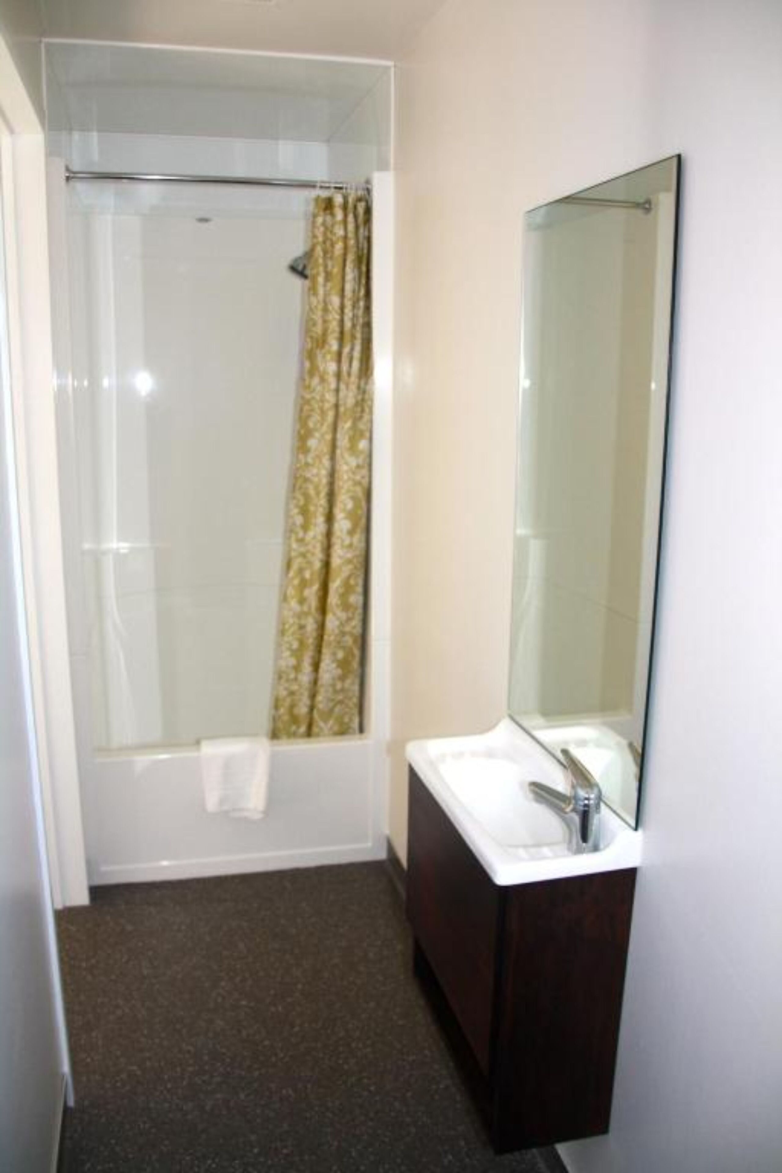 A bathroom with a glass shower enclosure, a wooden vanity with a mirror, and a towel hanging on the wall.