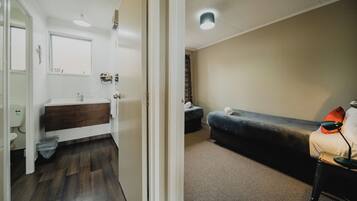 A room with a wooden floor, a white sink, a dark-colored couch, and a small table with a lamp.