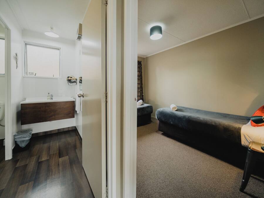 A room with a wooden floor, a white sink, a dark-colored couch, and a small table with a lamp.