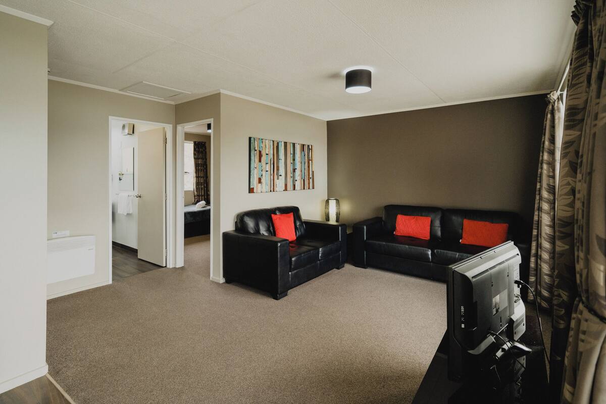 Un salon avec un canapé en cuir noir, un téléviseur à écran plat et un tableau accroché au mur.