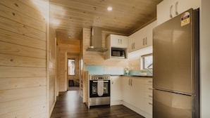 A modern kitchen with wooden walls, a stainless steel refrigerator, a built-in oven, and a microwave. - Lakes Edge Holiday Park (Lake Tekapo)