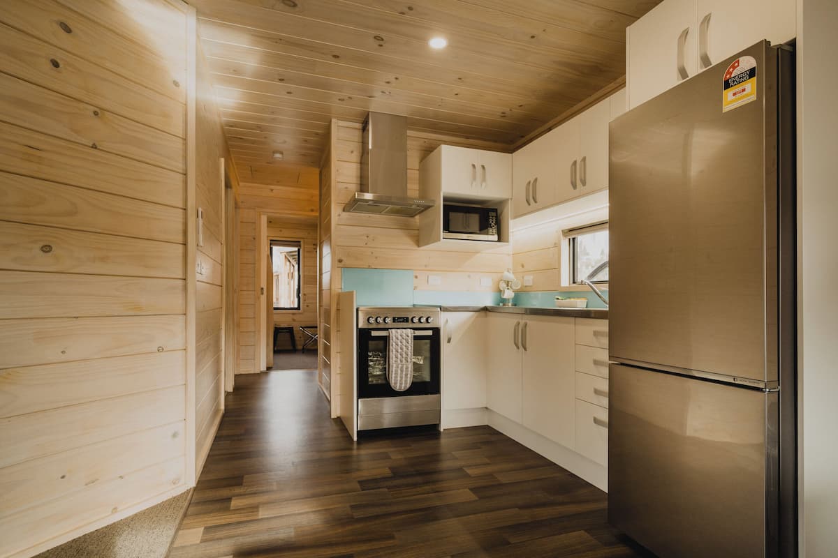 A modern kitchen with wooden walls, a stainless steel refrigerator, a built-in oven, and a microwave.