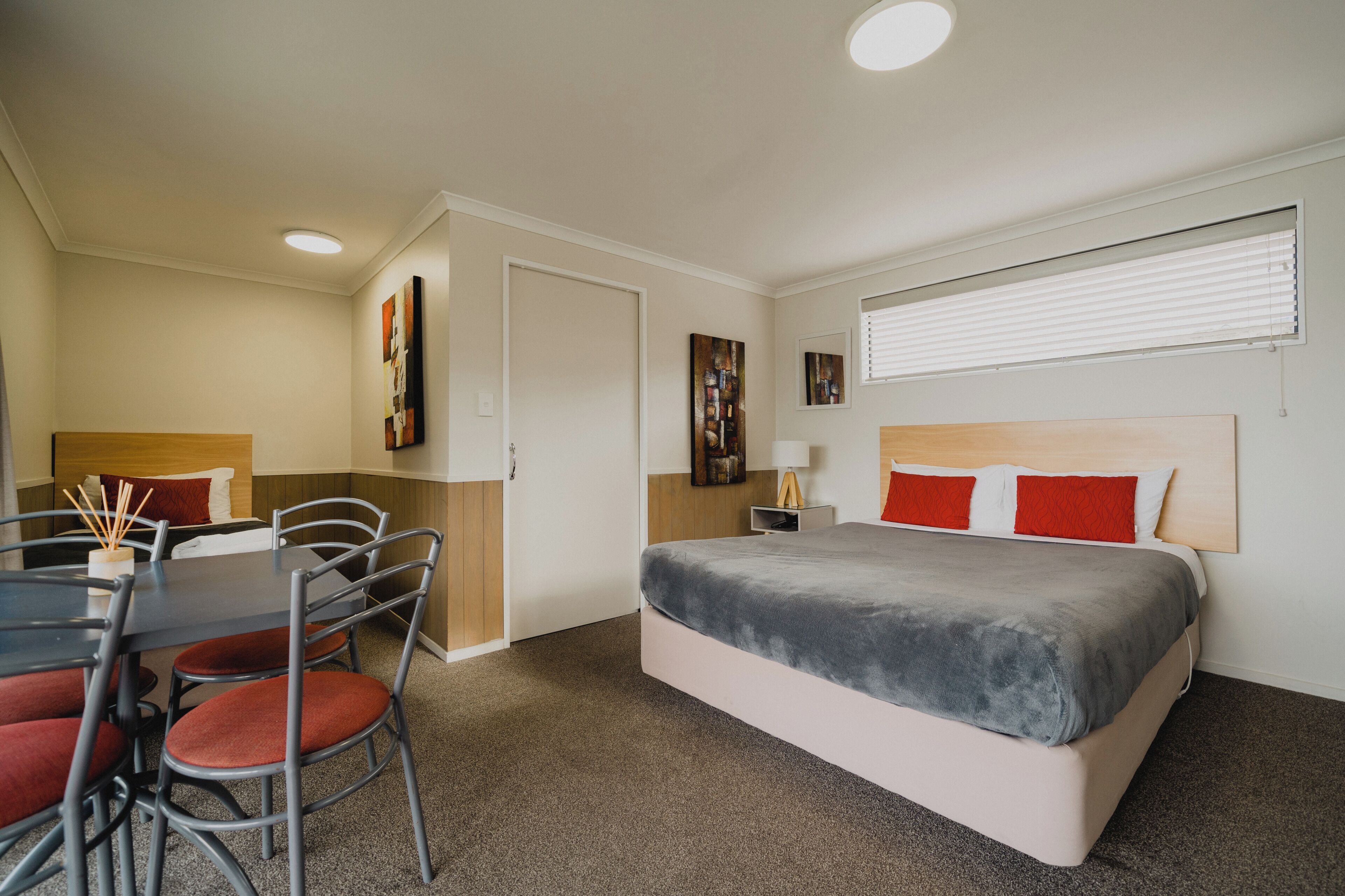 Una habitación de hotel con una cama, una mesa de comedor con sillas y una mesita de noche con lámpara.