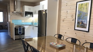 A modern kitchen with stainless steel appliances, wooden cabinetry, and a dining area with a glass table and chairs.