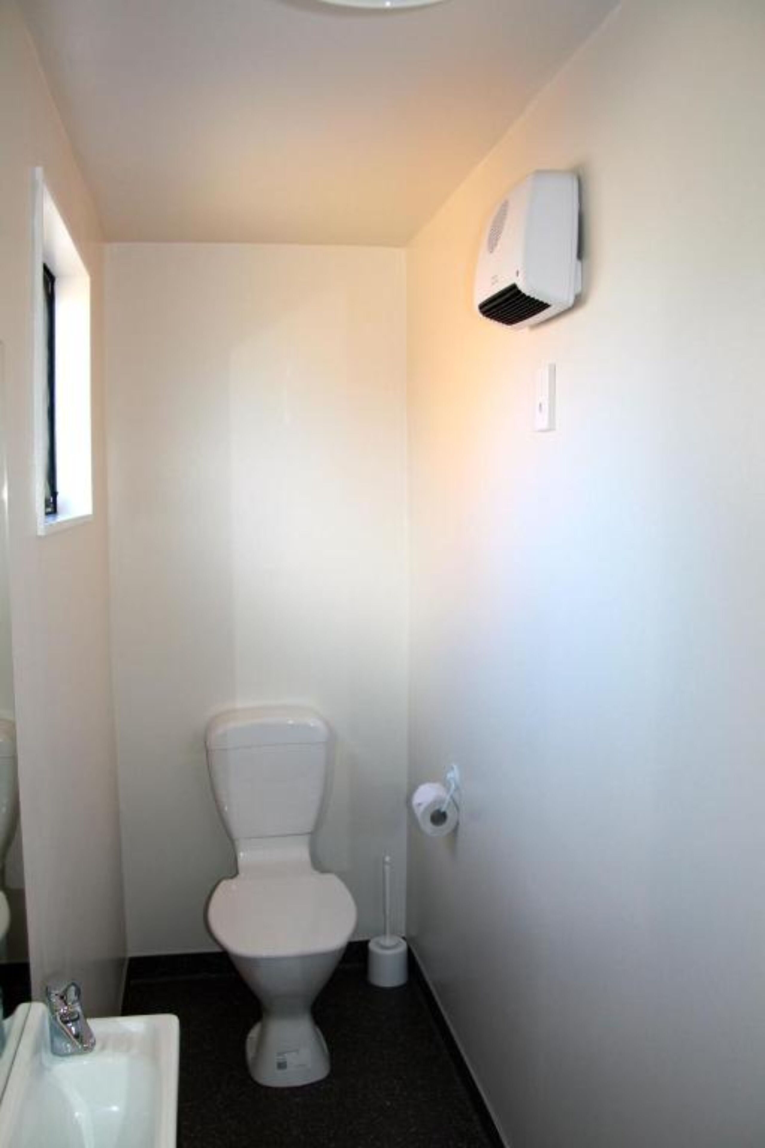 Une petite salle de bain propre, avec des toilettes blanches, un lavabo blanc et un climatiseur fixé au mur.