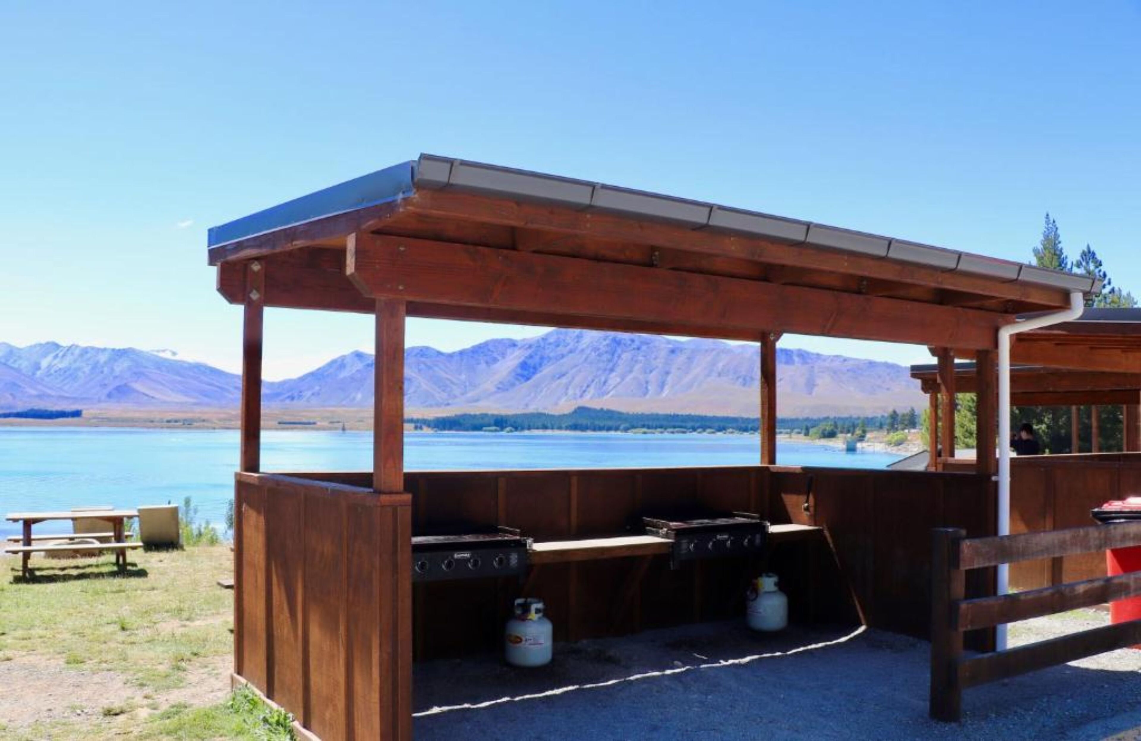 A wooden outdoor barbecue area with a view of mountains and a lake.