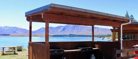 A wooden outdoor barbecue area with a view of mountains and a lake.