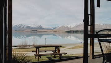 A wooden deck with a picnic table and a chair, overlooking a calm lake with mountains in the background.