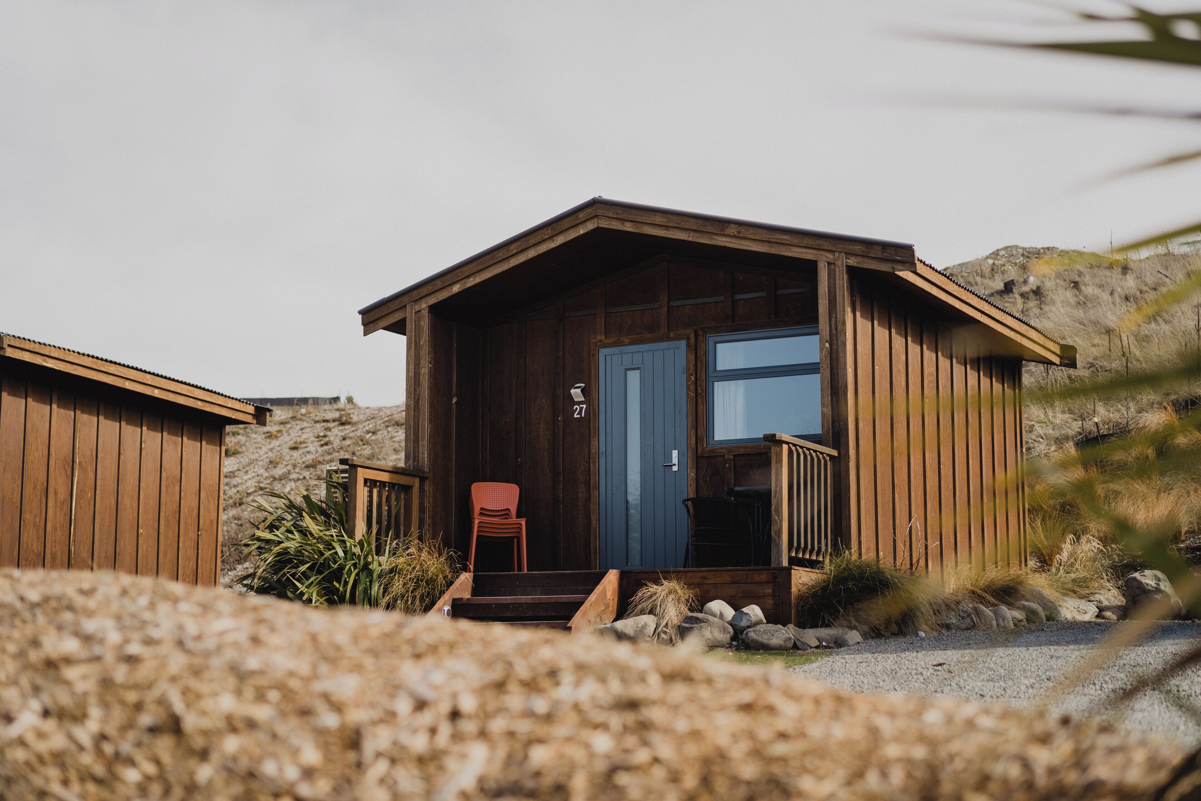 A wooden cabin with a porch, a door, and a number '27' on the door.