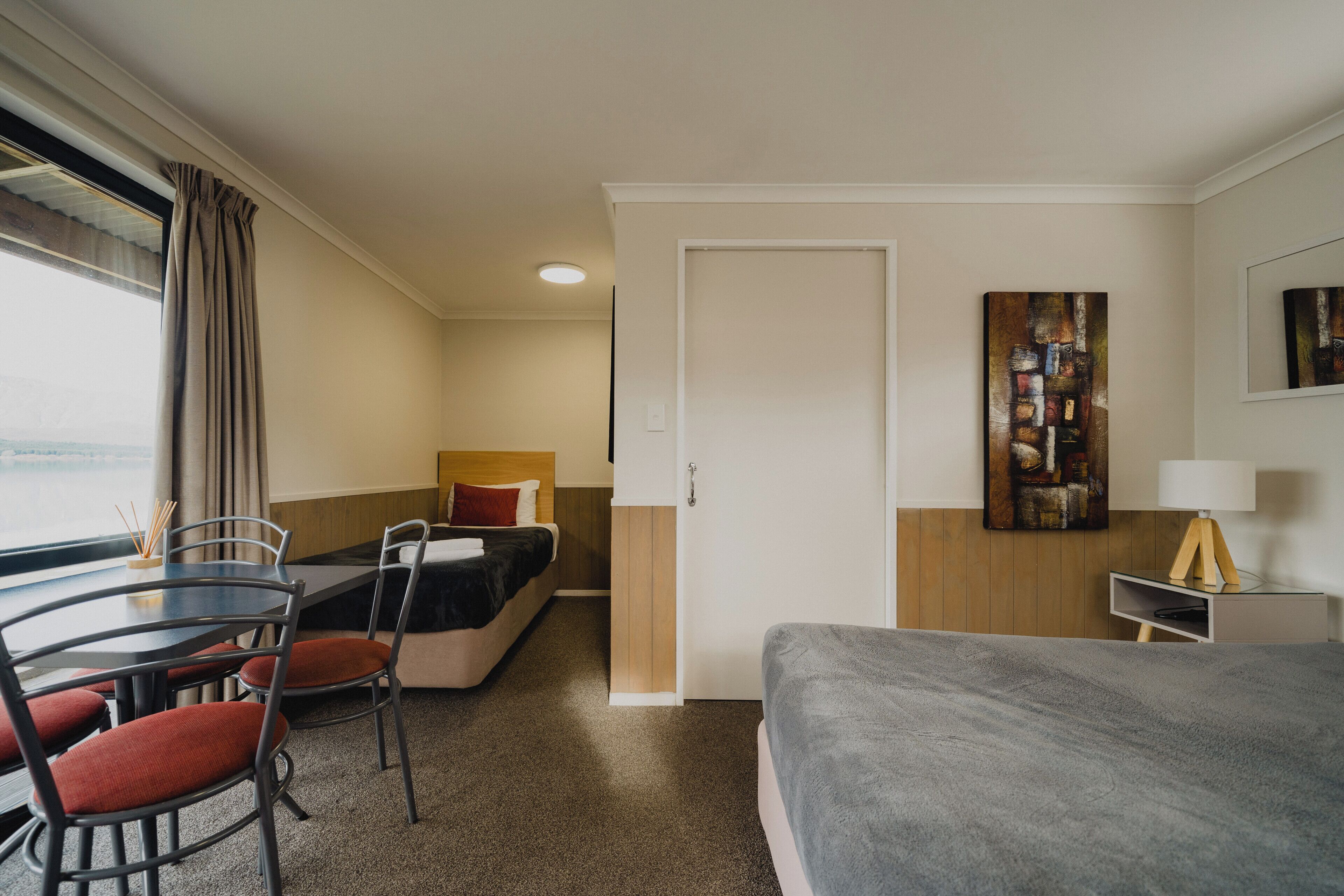 A hotel room with a bed, a desk with chairs, a dining table, and a painting on the wall.