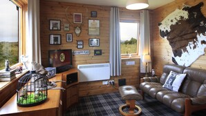 A cozy room with a leather sofa, a wooden desk with a birdcage, and a large wall-mounted animal hide. - Private Harry Potter themed lodge with lovely views (Arisaig)