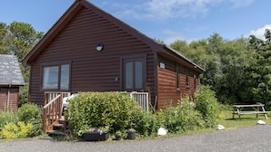 A wooden cabin with a porch, surrounded by greenery and a picnic table. - Private Star Wars themed lodge with lovely views (Arisaig)