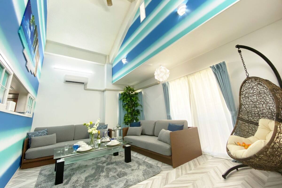 A modern living room with a glass coffee table, a sofa, a hanging chair, and a ceiling fan.