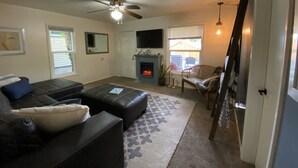 Un salon comprenant un canapé d’angle, une cheminée, un ventilateur de plafond et un téléviseur fixé au mur.