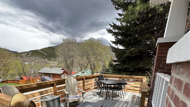 Une terrasse en bois aménagée avec du mobilier d’extérieur, notamment une table et des chaises, ainsi qu’un foyer.