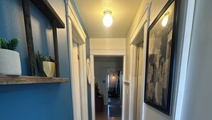 Un couloir avec un tapis à motifs, des étagères en bois ornées de plantes et un luminaire au plafond.
