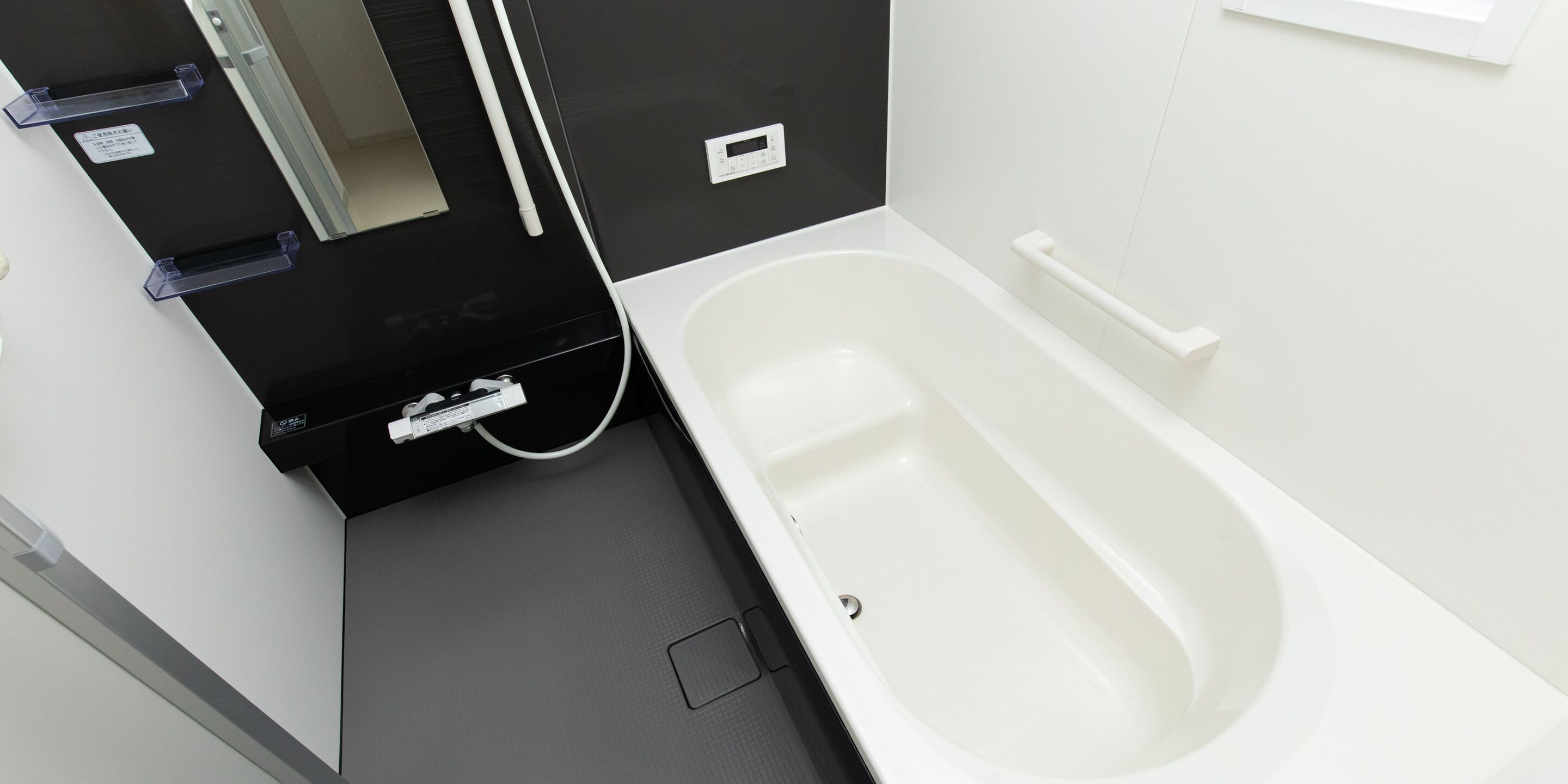 Un bagno moderno con una vasca da bagno bianca, un mobile lavabo nero con specchio e un portasciugamani bianco.