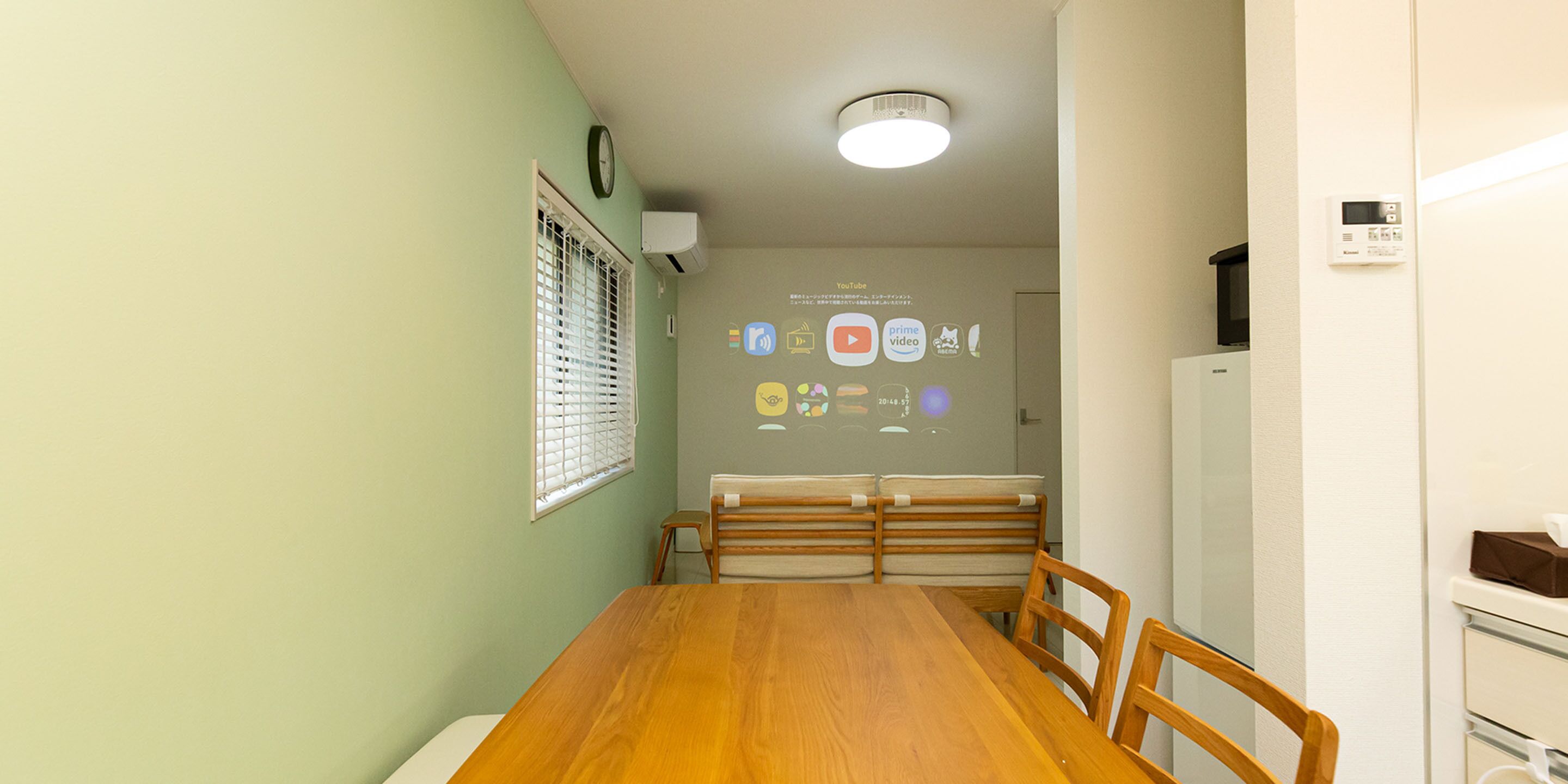 A dining area with a wooden table and chairs, a projection screen displaying icons, and a white refrigerator.