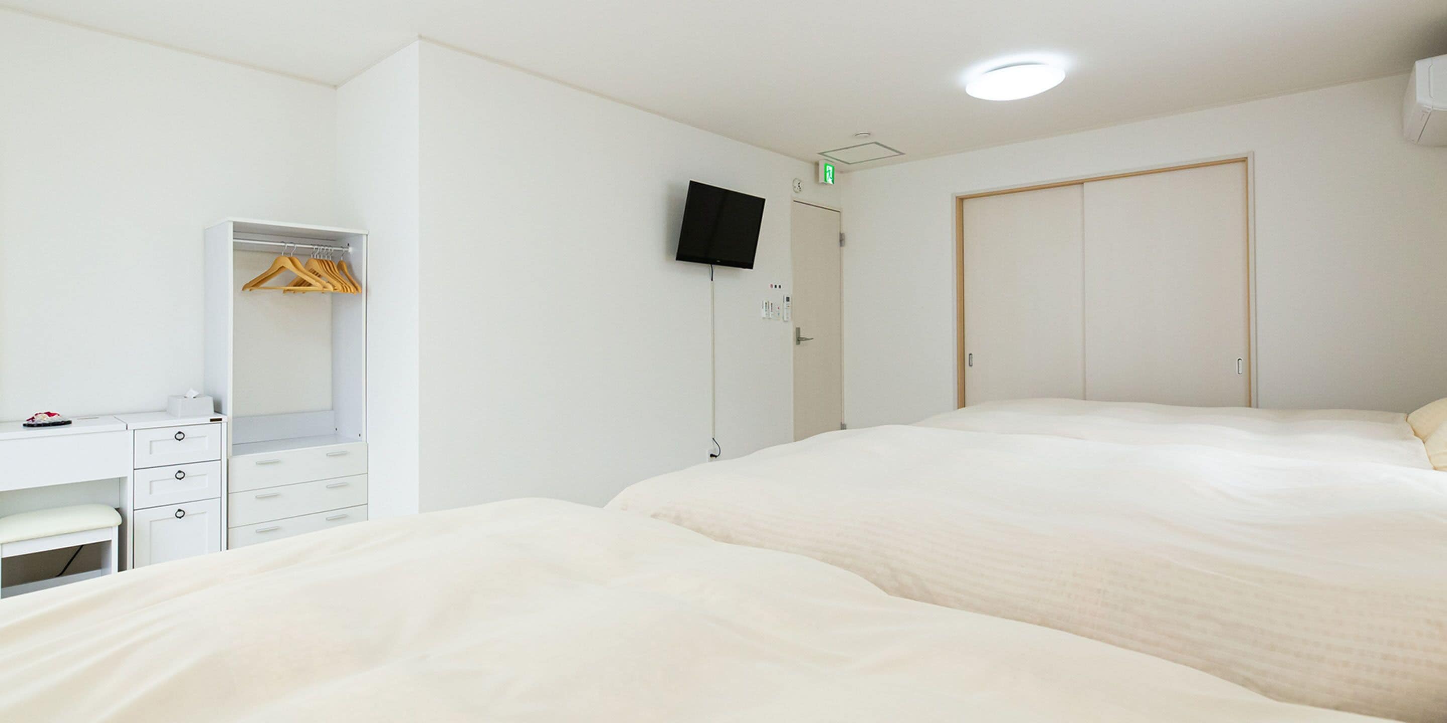 Een hotelkamer met een bed, een bureau met lades, een spiegel, een kledingkast en een televisie aan de muur.
